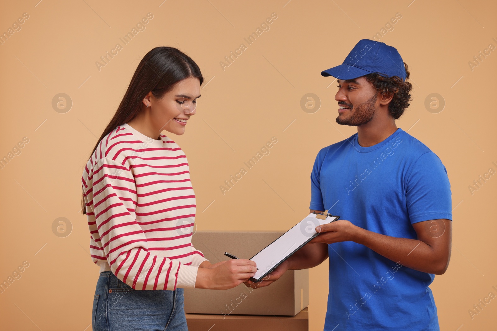 Photo of Smiling woman signing order receipt on light brown background. Courier delivery