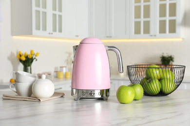 Photo of Modern electric kettle, tea set and apples on table in kitchen