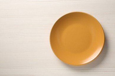 Photo of One orange ceramic plate on white wooden table, top view. Space for text