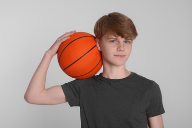 Teenage boy with basketball ball on light grey background
