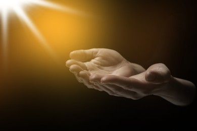 Image of Christian woman stretching hands towards holy light in darkness, closeup. Prayer and belief