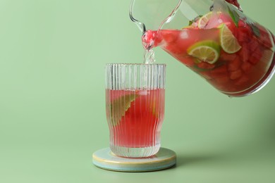 Photo of Pouring tasty summer watermelon drink with lime from jug into glass on pale light green background