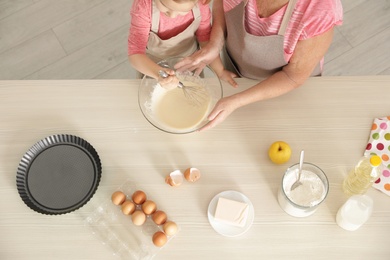 Little girl and her grandmother cooking at table with products, top view