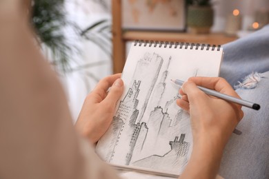 Image of Woman sketching cityscape in notebook with pencil at home, closeup
