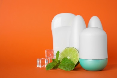 Photo of Natural roll-on deodorants, mint, lime and ice on orange background, space for text