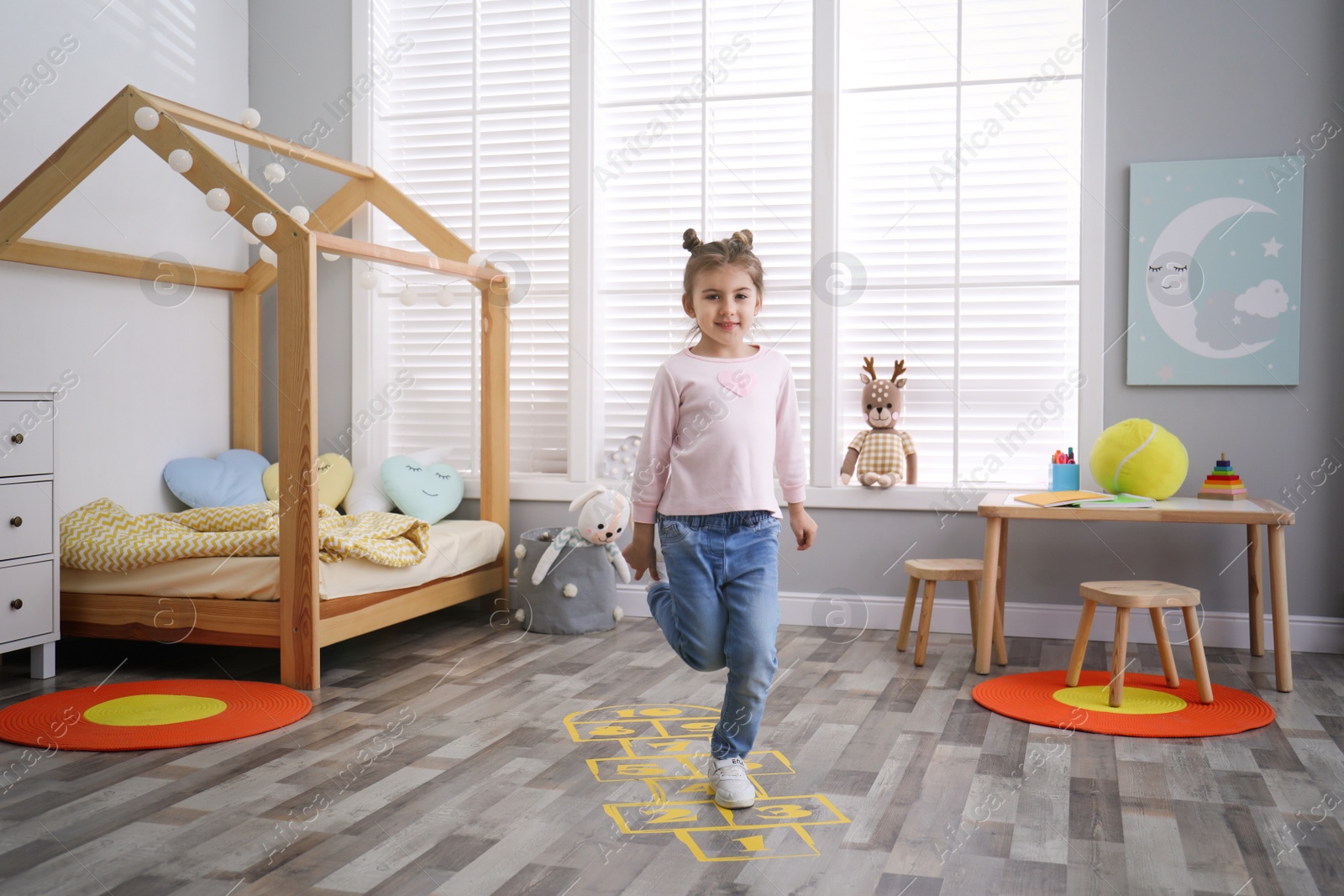 Photo of Cute little girl playing hopscotch at home