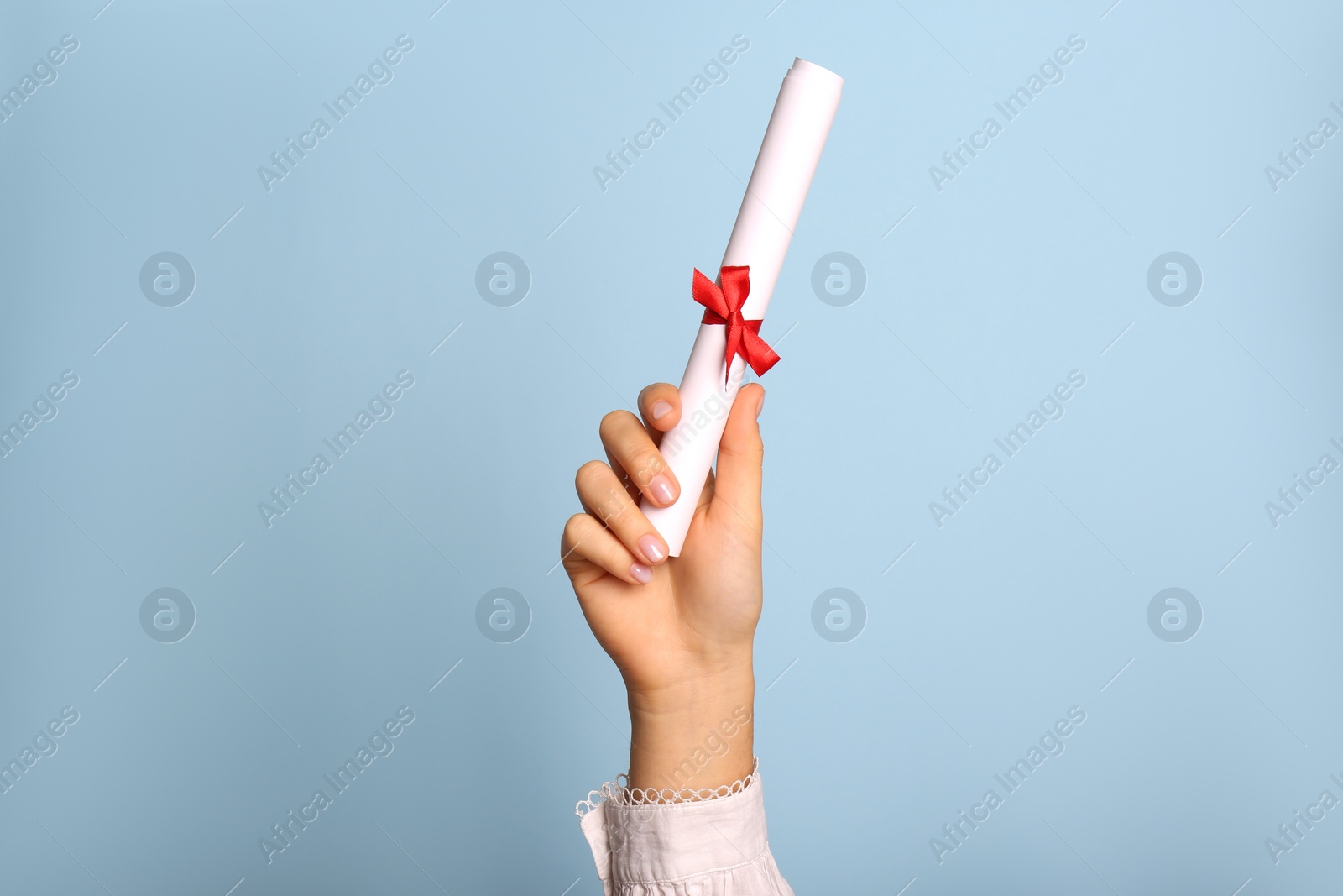 Photo of Student holding rolled diploma with red ribbon on light blue background, closeup