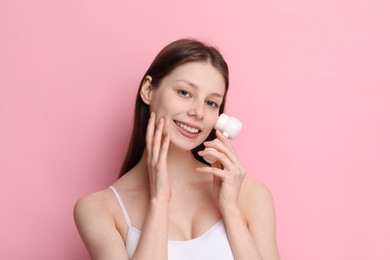 Washing face. Young woman with cleansing brush on pink background