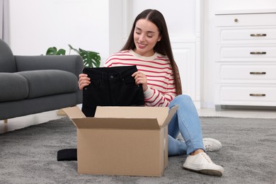 Photo of Happy young woman taking black jeans out of box at home. Online shopping