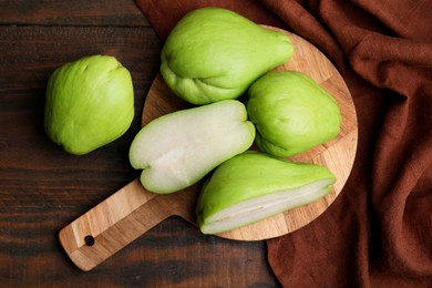 Cut and whole chayote on wooden table, flat lay