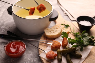 Photo of Fondue pot, forks with fried meat pieces, ketchup and other products on grey textured table