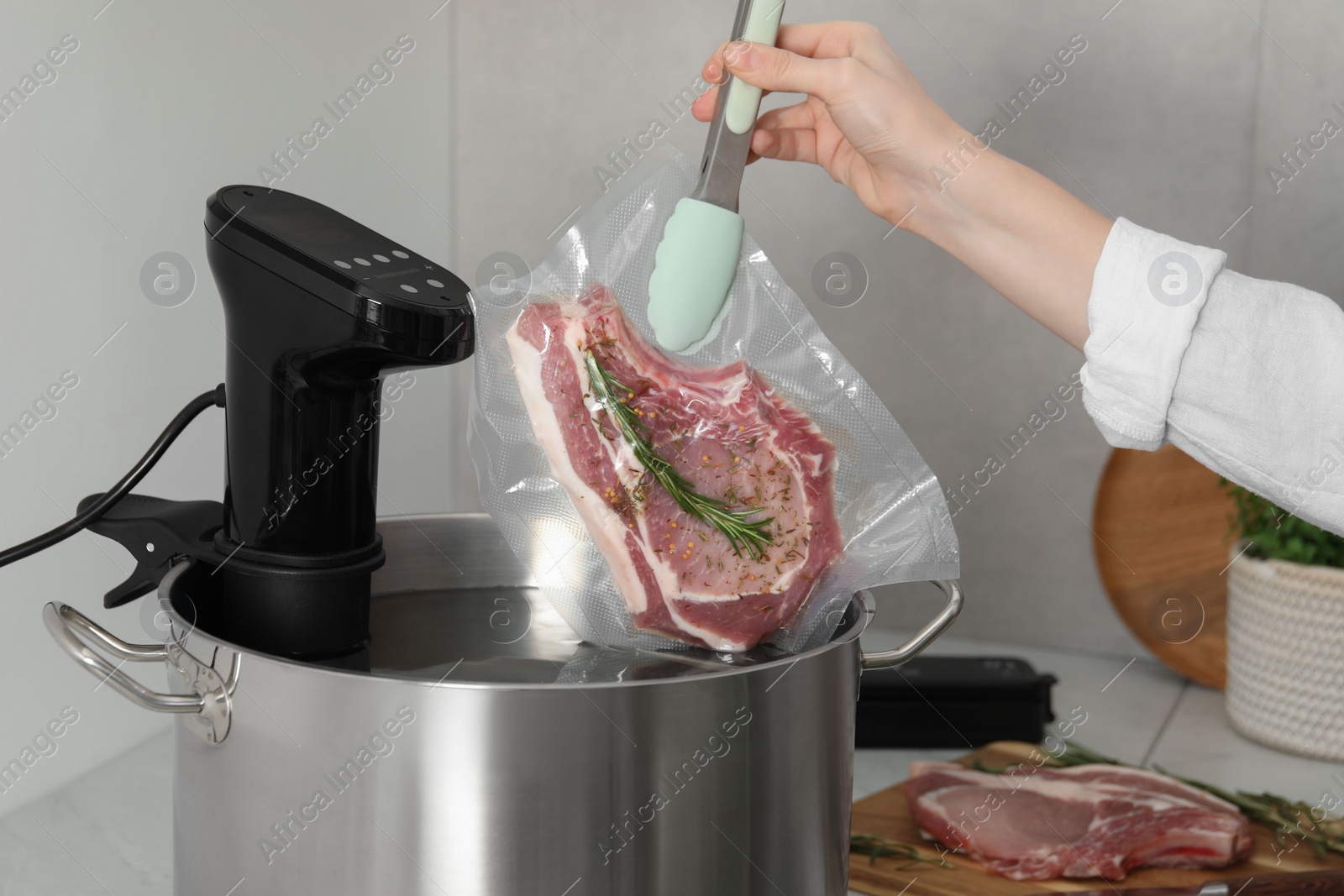 Photo of Woman putting vacuum packed meat into pot with sous vide cooker in kitchen, closeup. Thermal immersion circulator