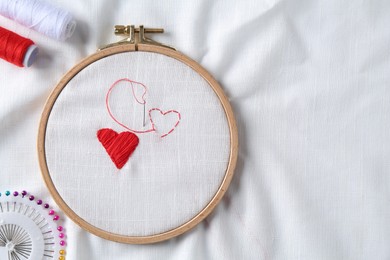 Embroidered red hearts, needle and tools on white cloth, flat lay. Space for text