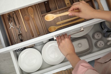 Photo of Woman taking wooden spoon from drawer of kitchen cabinet, top view