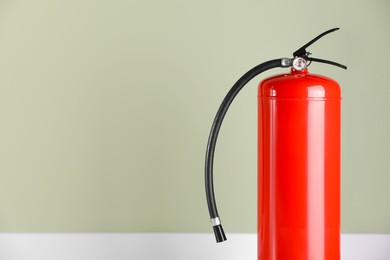 Fire extinguisher near pale green wall, space for text