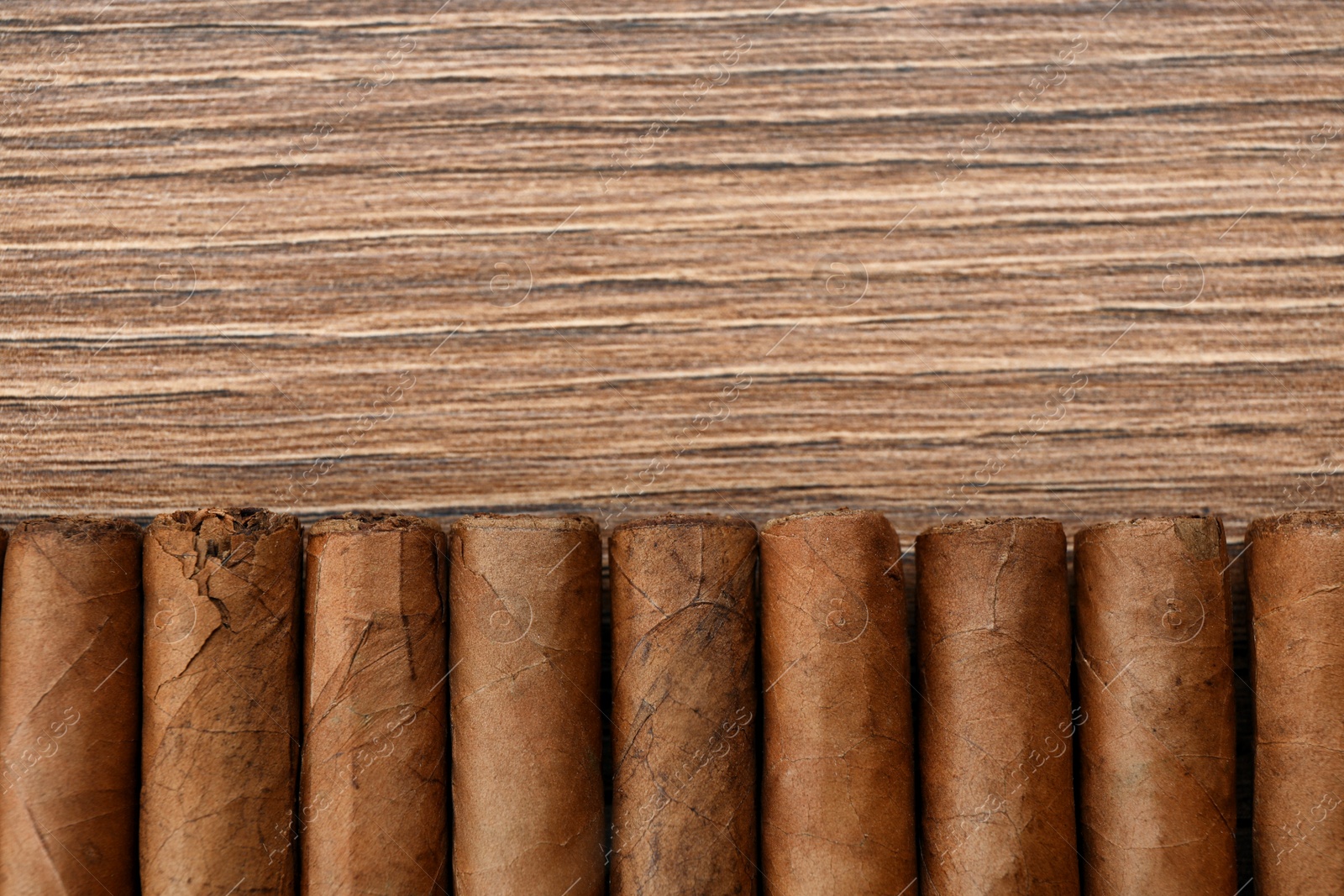 Photo of Cigars wrapped in tobacco leaves on wooden table, flat lay. Space for text