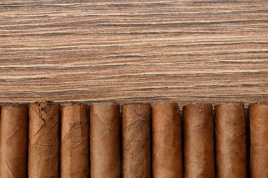 Photo of Cigars wrapped in tobacco leaves on wooden table, flat lay. Space for text