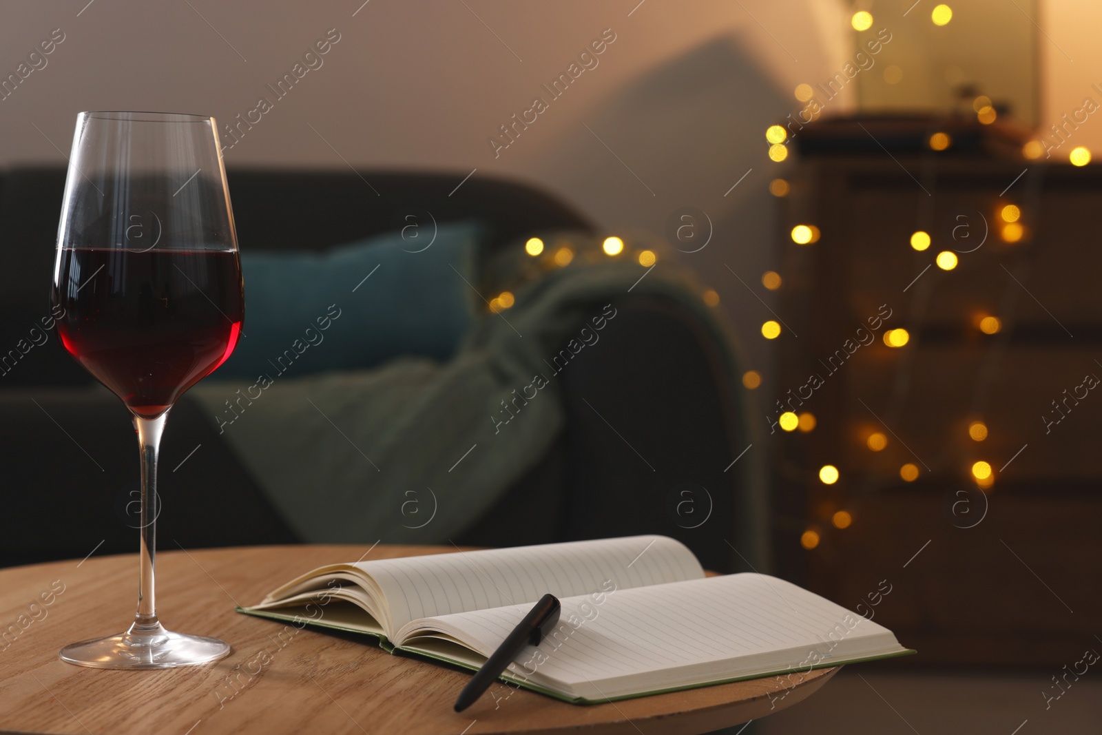 Photo of Glass of red wine and open notebook with pen on wooden table in room. Relax at home