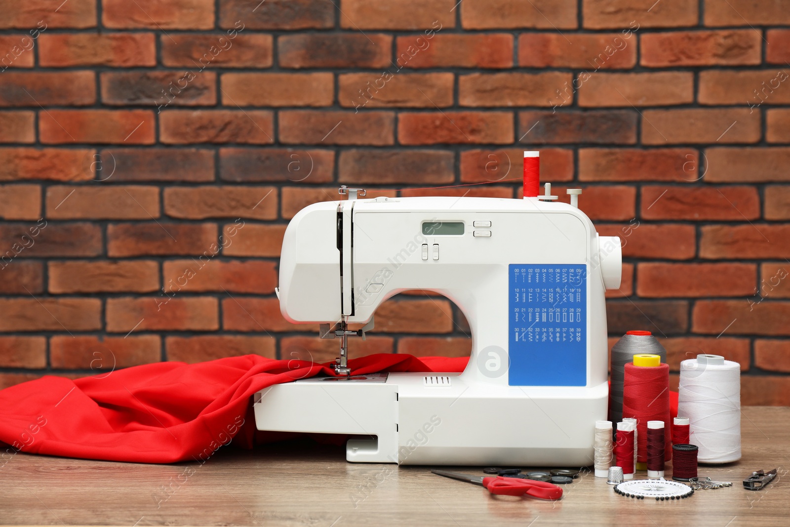 Photo of Sewing machine with fabric and craft accessories on wooden table against brick wall