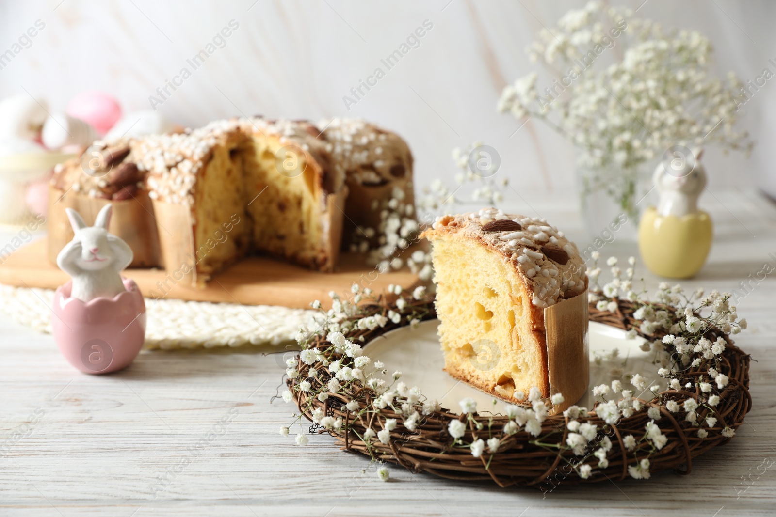 Photo of Delicious Italian Easter dove cake (traditional Colomba di Pasqua) in nest and festive decor on white wooden table, space for text