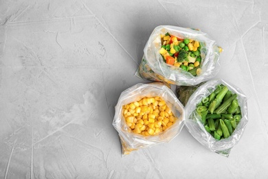 Plastic bags with different frozen vegetables on table, top view