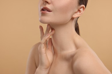 Woman touching her neck on beige background, closeup