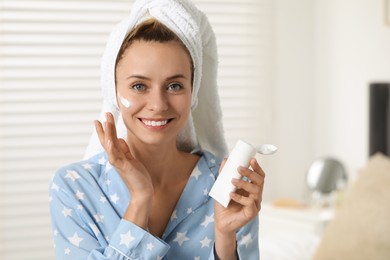 Photo of Young woman applying cream onto her face at home, space for text. Spa treatments