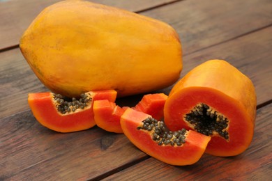 Photo of Ripe cut and whole papaya fruits on wooden table