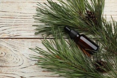 Glass bottle of essential oil and pine branches with cones on white wooden table, flat lay. Space for text