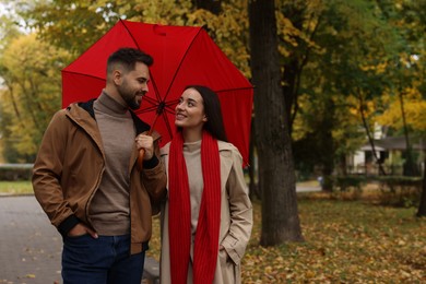 Photo of Happy young couple with red umbrella spending time together in autumn park, space for text