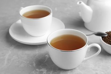 Photo of Cups of buckwheat tea and granules on light grey marble table