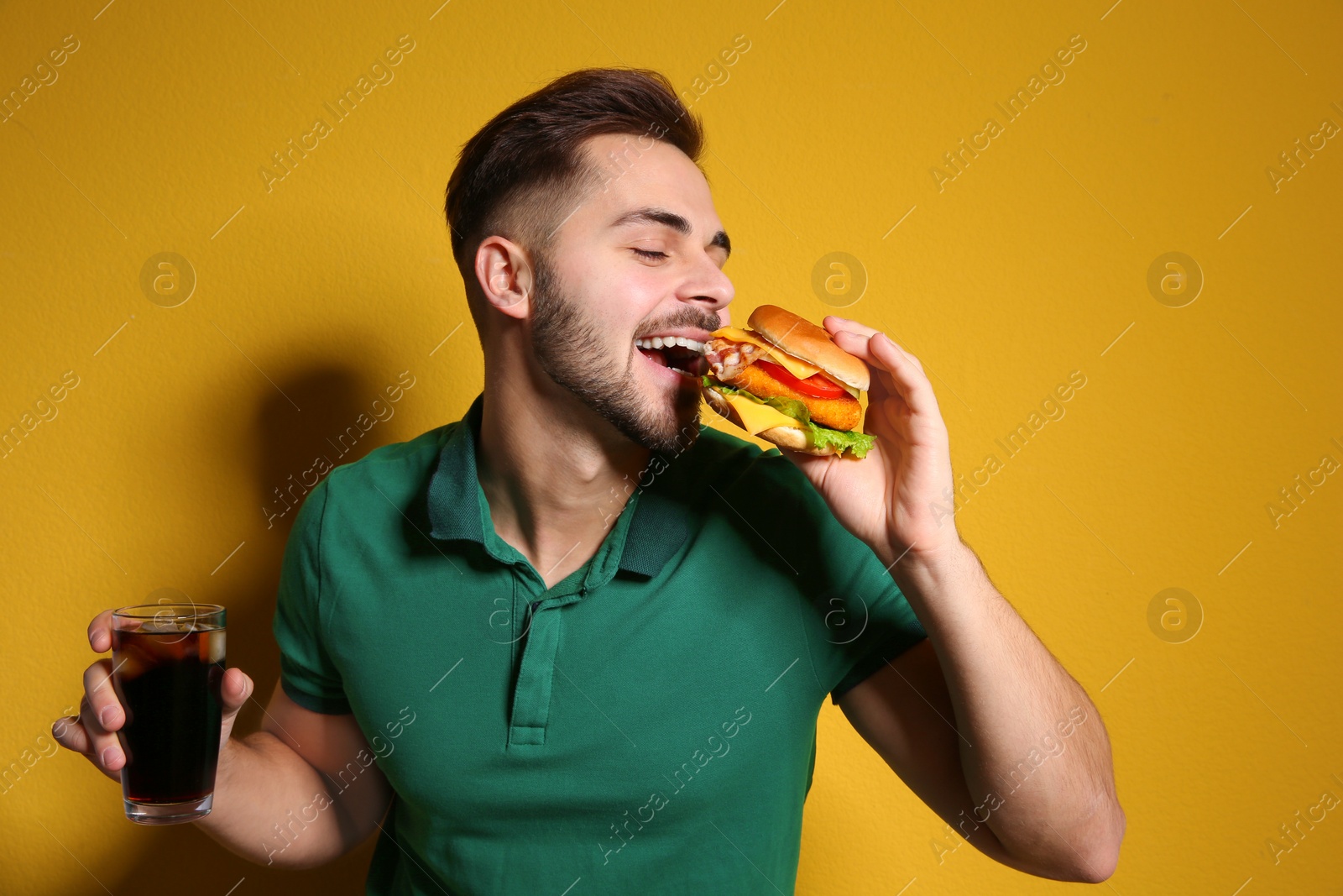 Photo of Handsome man with tasty burger and cola on color background