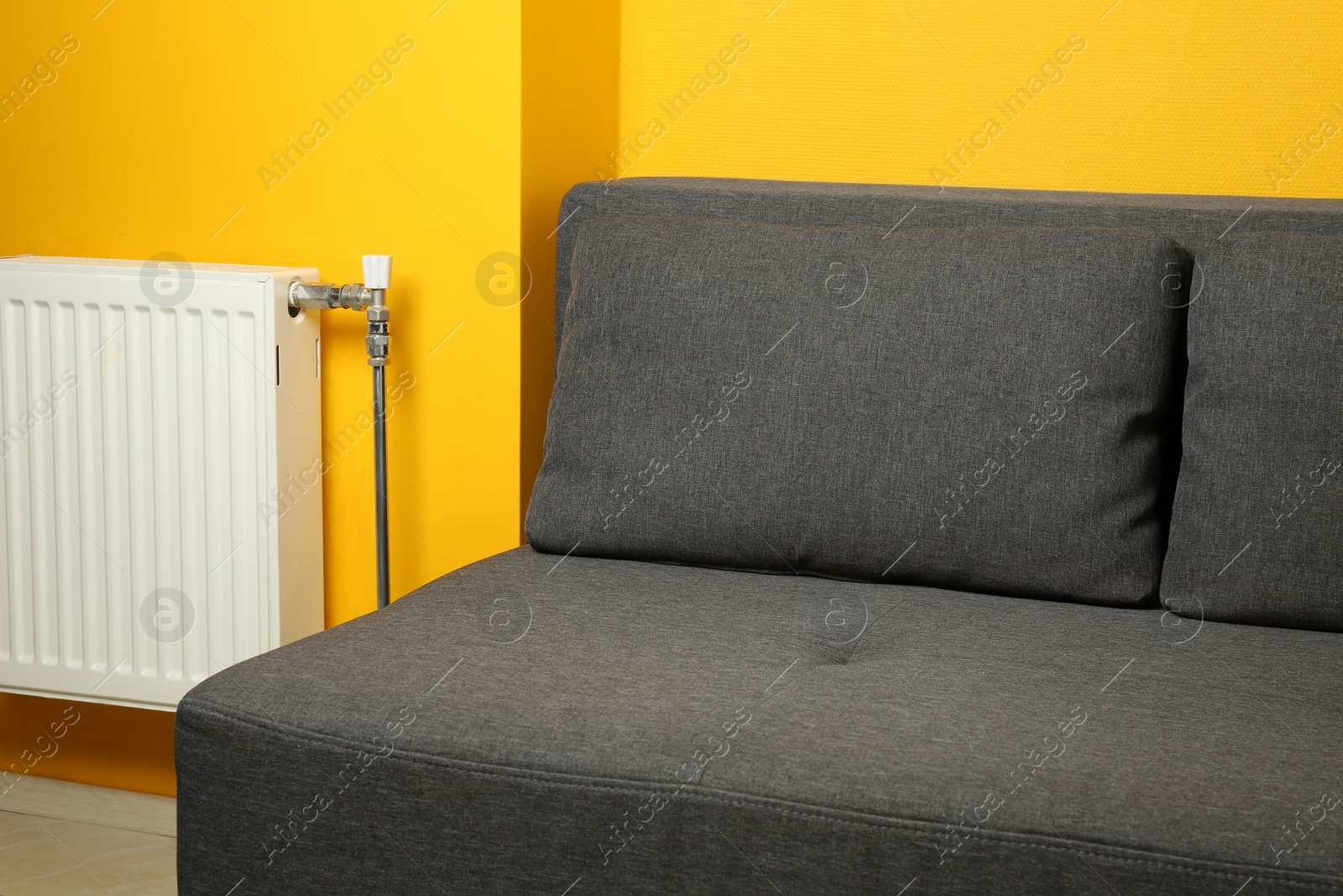 Photo of Stylish grey sofa near yellow wall in room