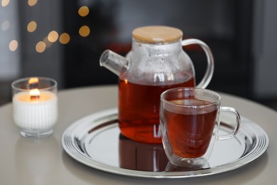 Photo of Teapot, cup of aromatic tea and burning candle on white table indoors, space for text