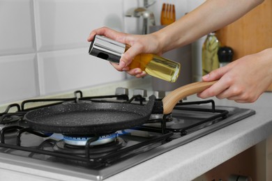 Photo of Woman spraying cooking oil onto frying pan on gas stove, closeup