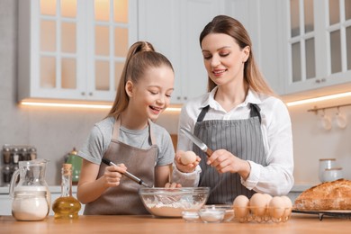 Photo of Making bread. Mother and her daughter preparing dough at wooden table in kitchen