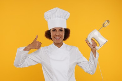 Photo of Happy female chef in uniform holding mixer and showing thumb up on white background
