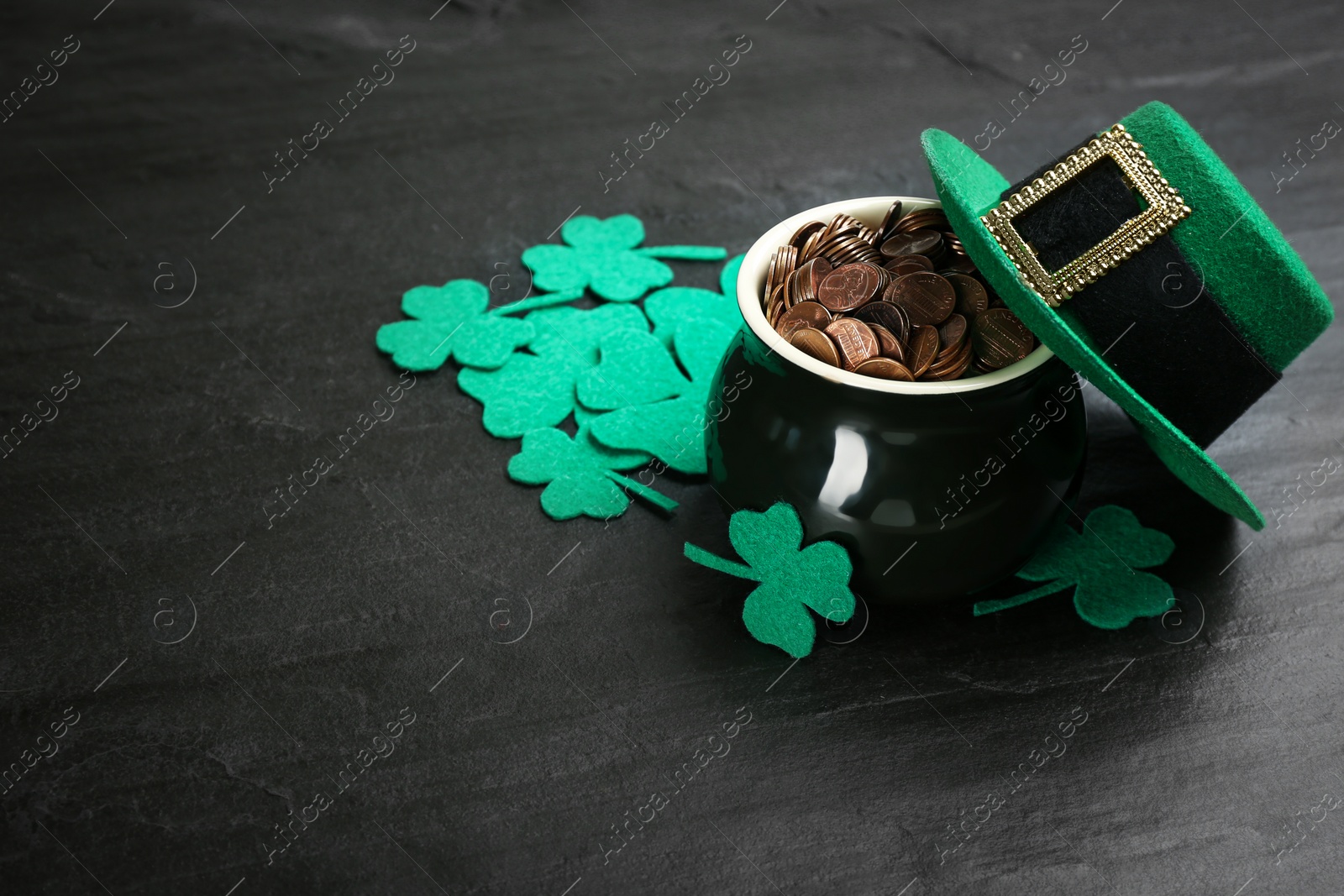 Photo of Pot of gold coins, hat and clover leaves on black stone table, space for text. St. Patrick's Day celebration