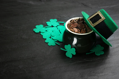 Pot of gold coins, hat and clover leaves on black stone table, space for text. St. Patrick's Day celebration