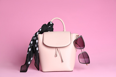 Photo of Stylish woman's backpack, scarf and sunglasses on light pink background