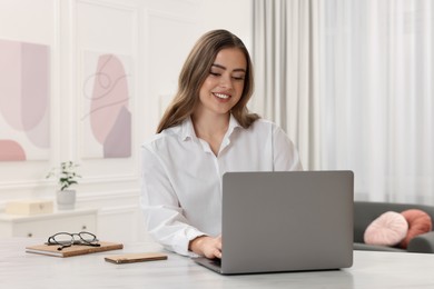 Happy woman with laptop at white table in room