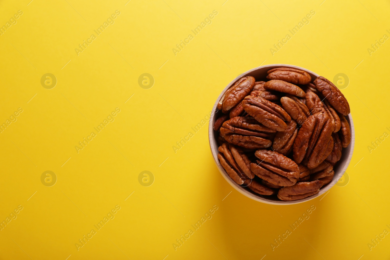 Photo of Tasty pecan nuts in bowl on yellow background, top view. Space for text