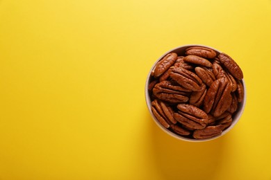 Tasty pecan nuts in bowl on yellow background, top view. Space for text