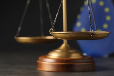Photo of Scales of justice on grey table near European Union flag, closeup
