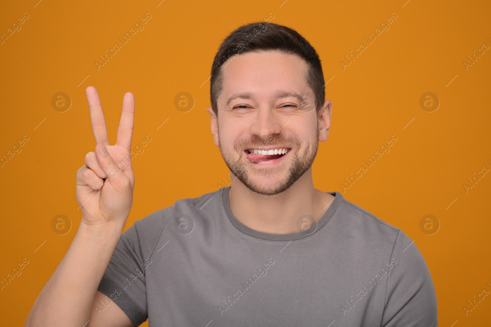 Photo of Happy man showing his tongue and V-sign on orange background