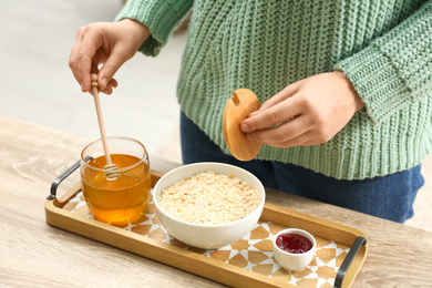 Woman adding honey to oatmeal at wooden table indoors, closeup