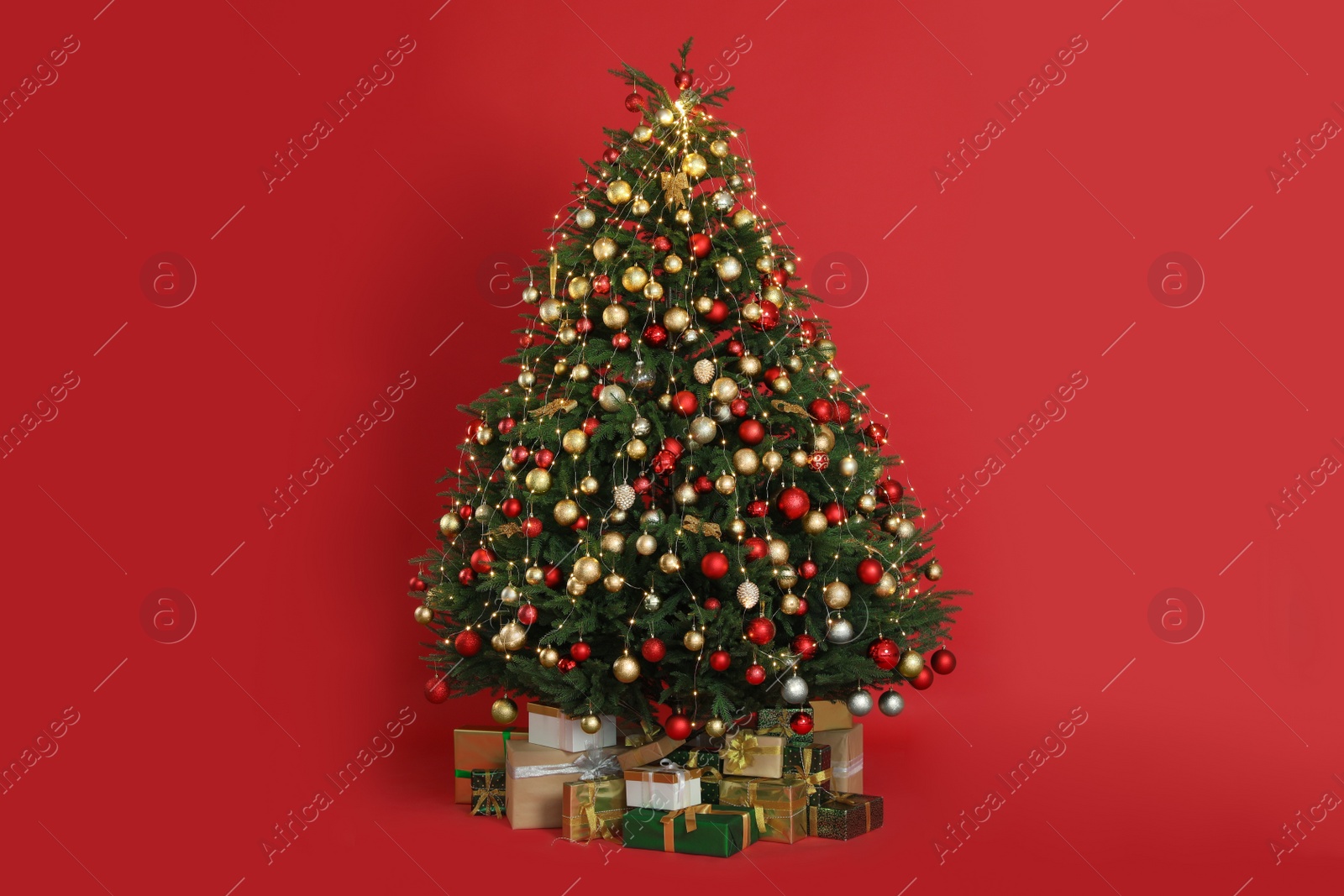 Photo of Beautifully decorated Christmas tree and many gift boxes on red background