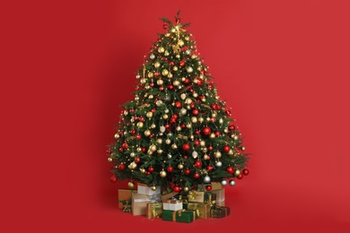 Photo of Beautifully decorated Christmas tree and many gift boxes on red background