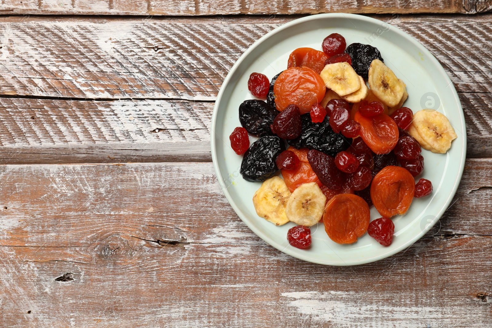 Photo of Mix of delicious dried fruits on wooden table, top view. Space for text