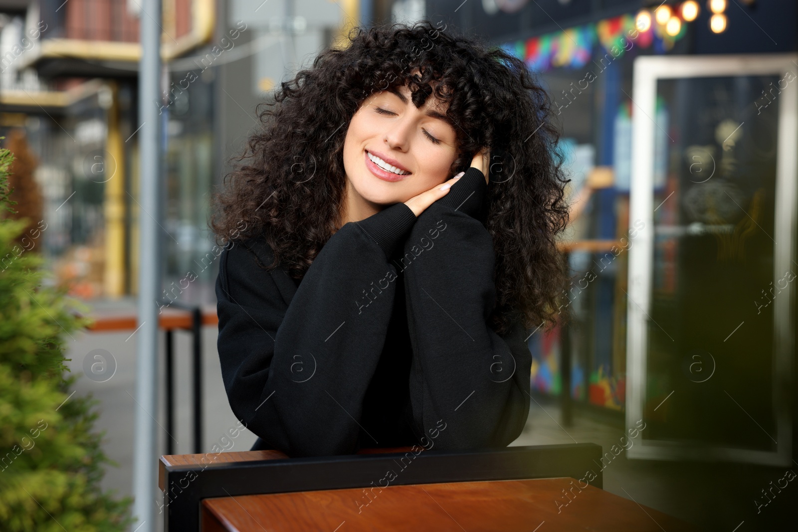 Photo of Happy young woman in stylish black sweater at wooden table outdoors